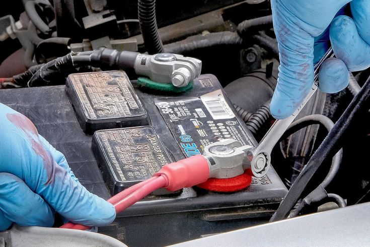 Mechanic wearing protective gloves removing a car battery from the engine bay